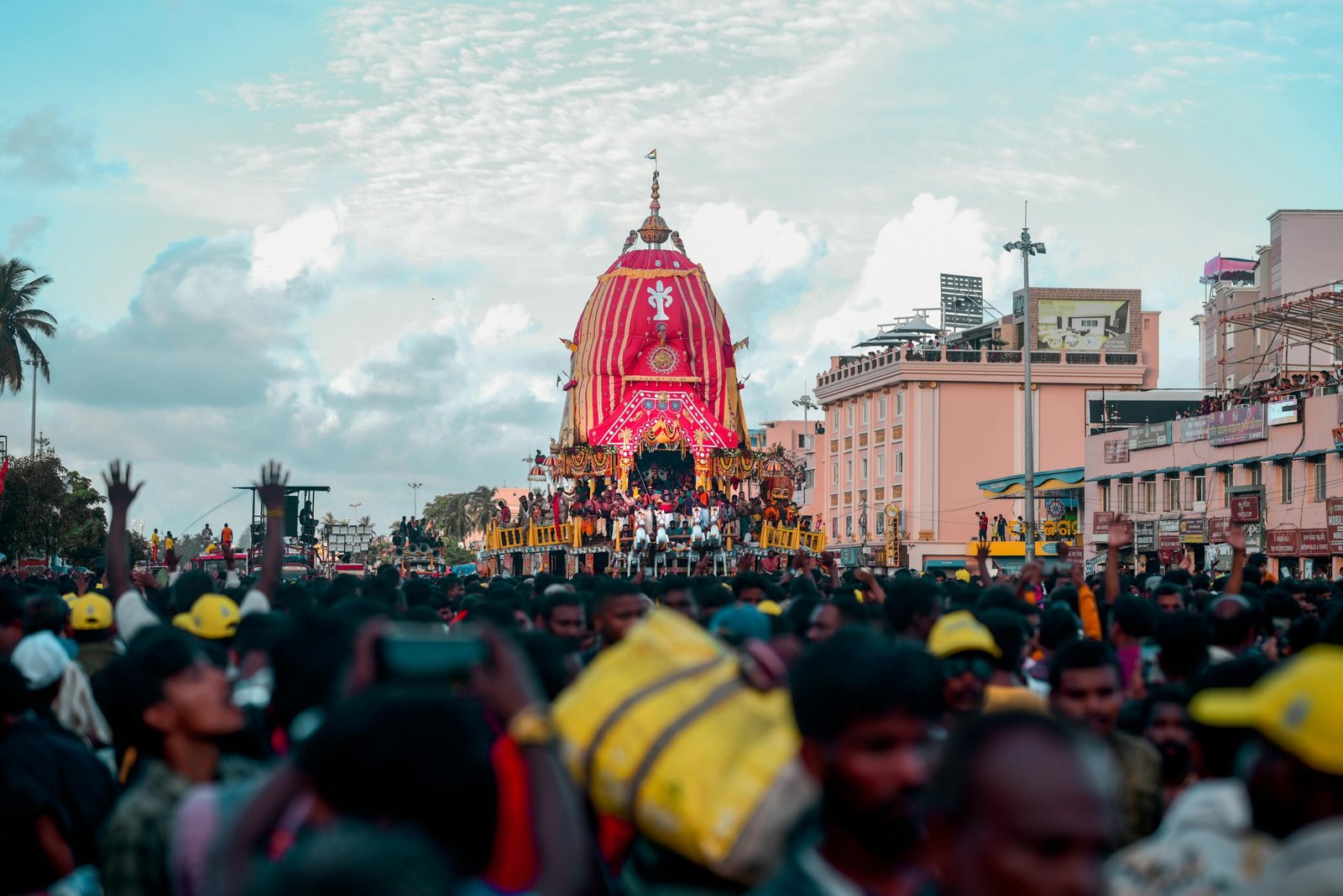 A colorful and lively street festival featuring a decorated chariot surrounded by a large crowd.